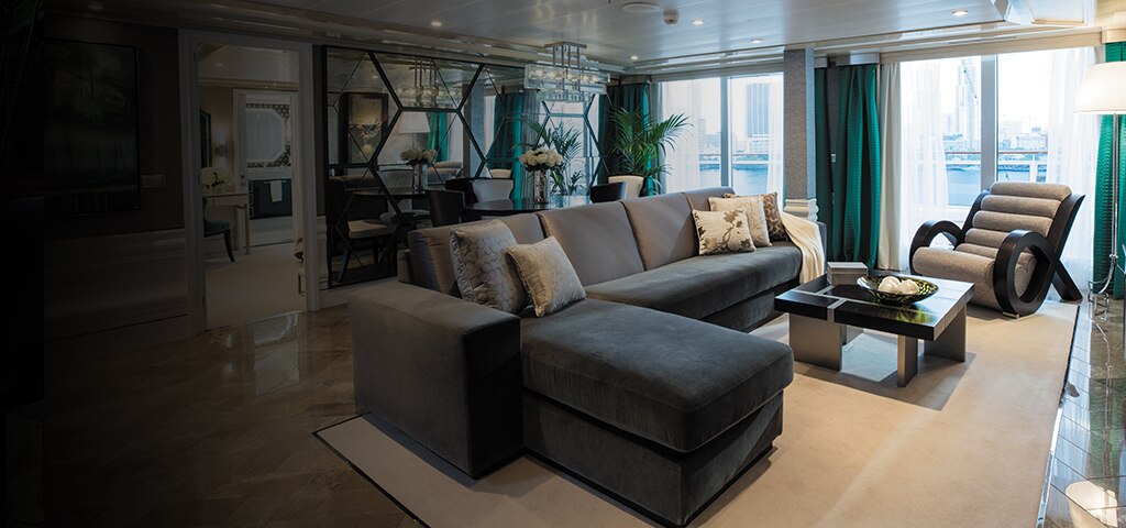inside luxurious cruise suite living room with teal and gray decor and balcony