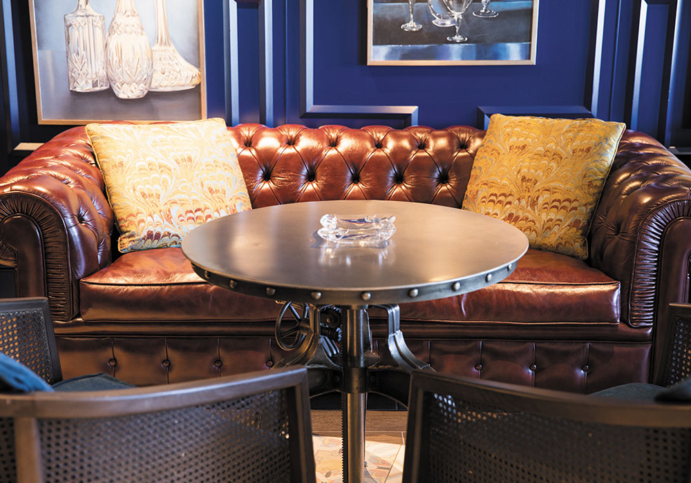 connoisseur club is decorated with a brown leather sofa, blue walls and metal table